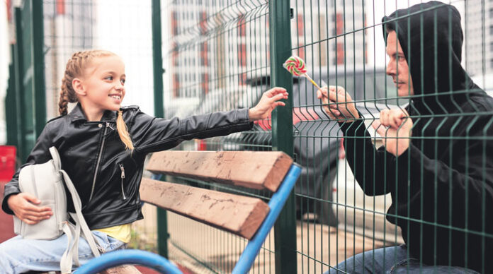 Stranger offers candy to child sitting on playground. Kid in danger.